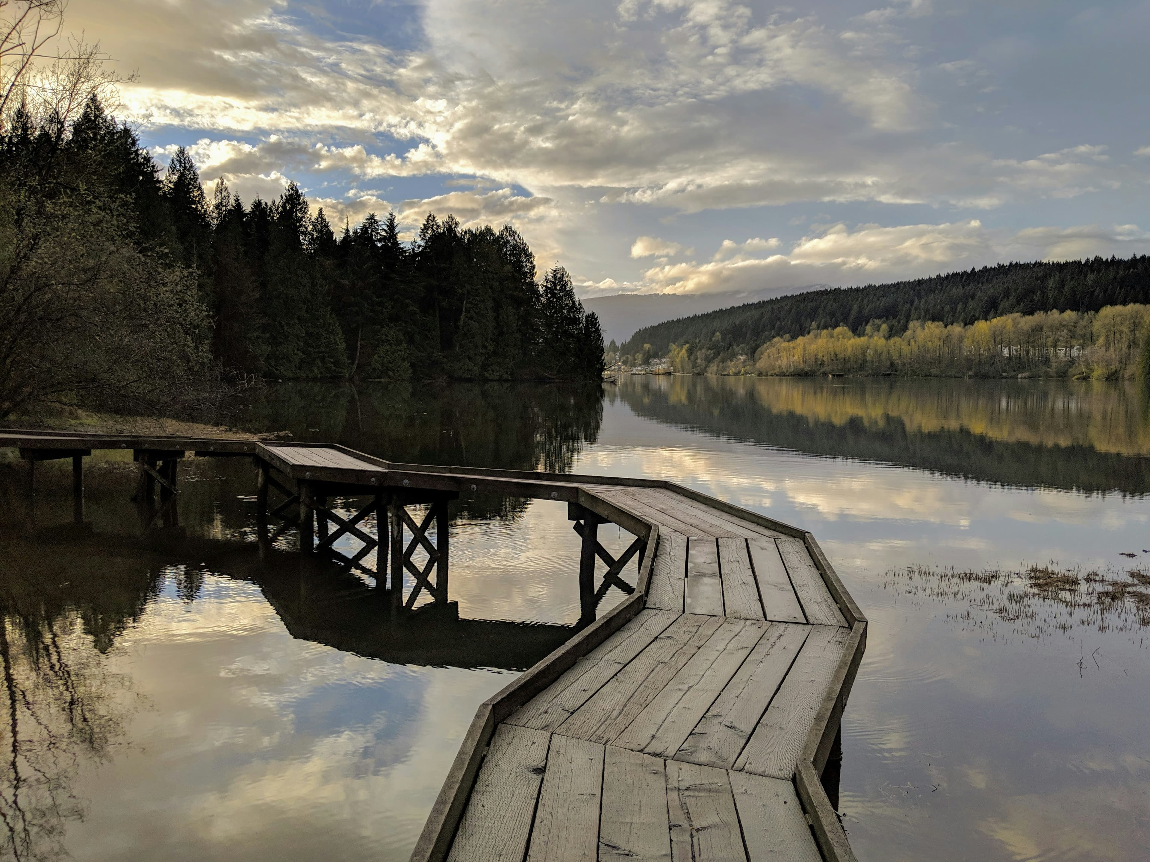 A wooden waterfront dock surrounded by trees and mountain scenery in Port Moody, British Columbia.
